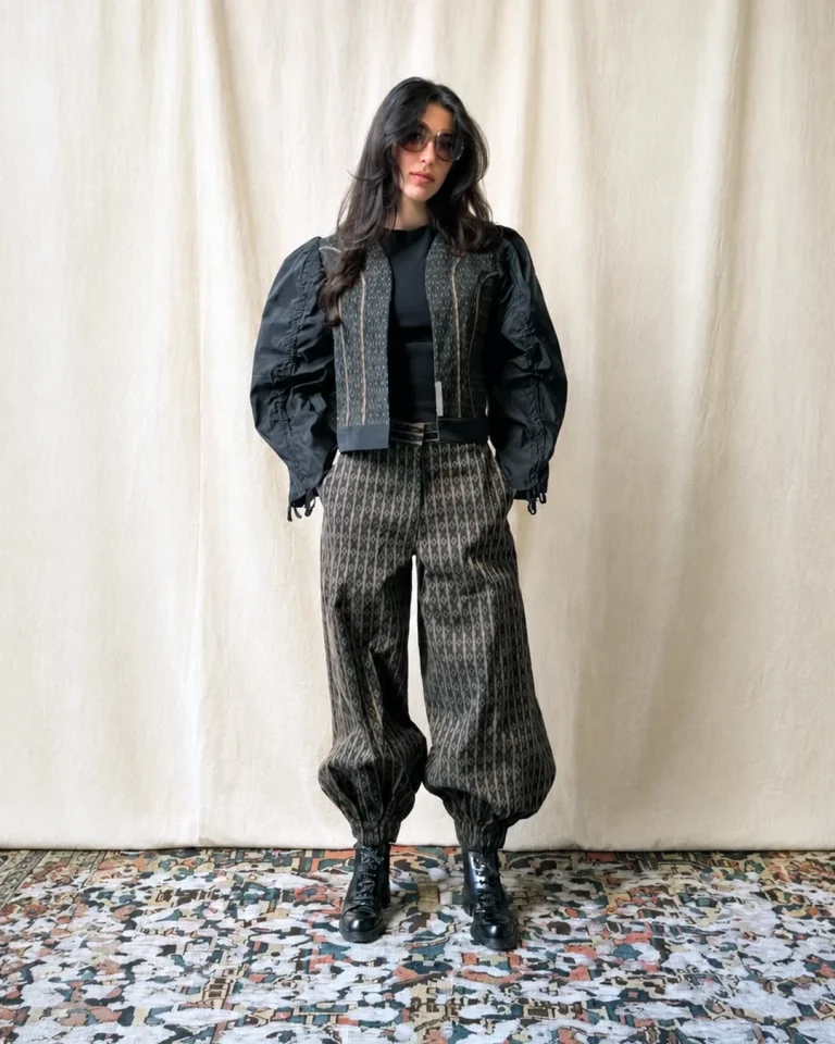Full-length indoor view of the Fika Jacket and Trousers, featuring a cropped black patterned jacket, voluminous sleeves, relaxed cuffed trousers, black boots, and sunglasses