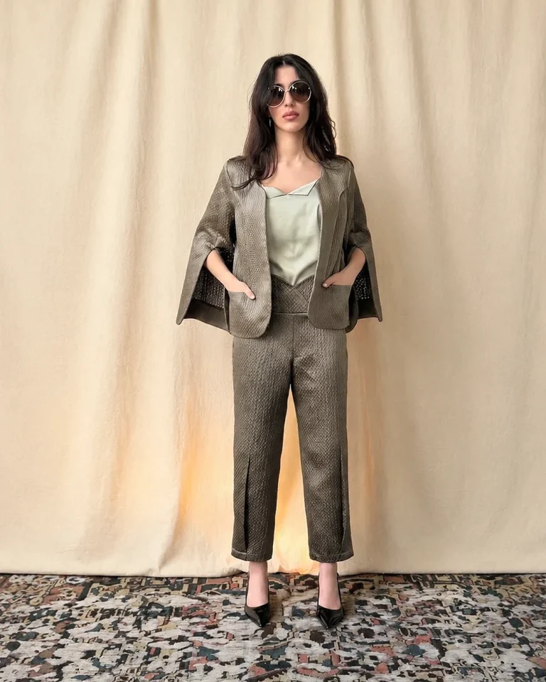 Full-length indoor view of the Sedar Jacket and Trousers, featuring a short relaxed embossed taffeta jacket, a light-toned top, straight trousers, and black heels
