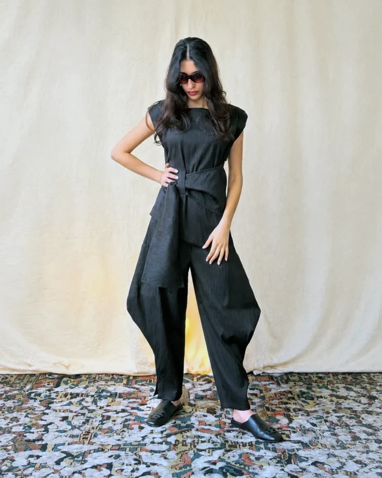 Full-body front view of the Tifon pleated taffeta set, featuring vertical pleats, wide-volume trousers, and an asymmetric top