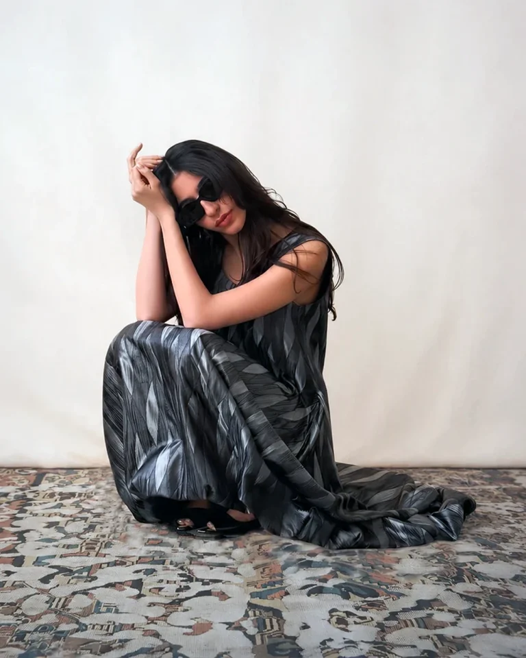Seated view of the Silver Silk Dress, emphasizing the soft drape, sculptural folds, and charcoal-silver sheen of the fabric