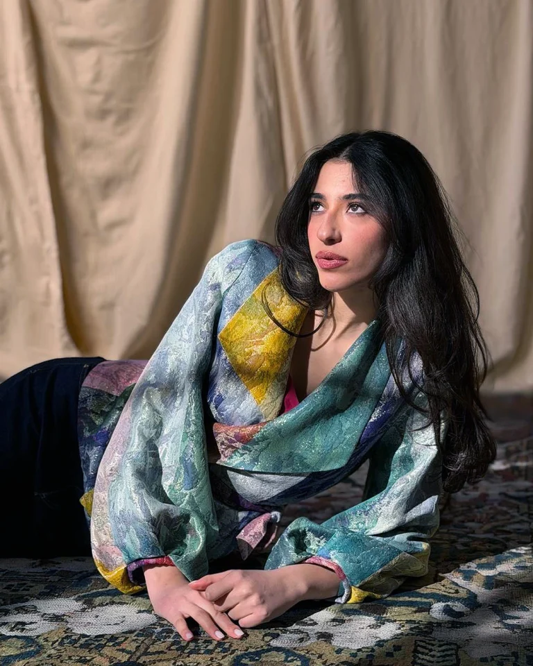 Reclining view of the Zarvan Handwoven Jacket, highlighting the handwoven texture, puff sleeves, cross-over front, and reflective textile surface