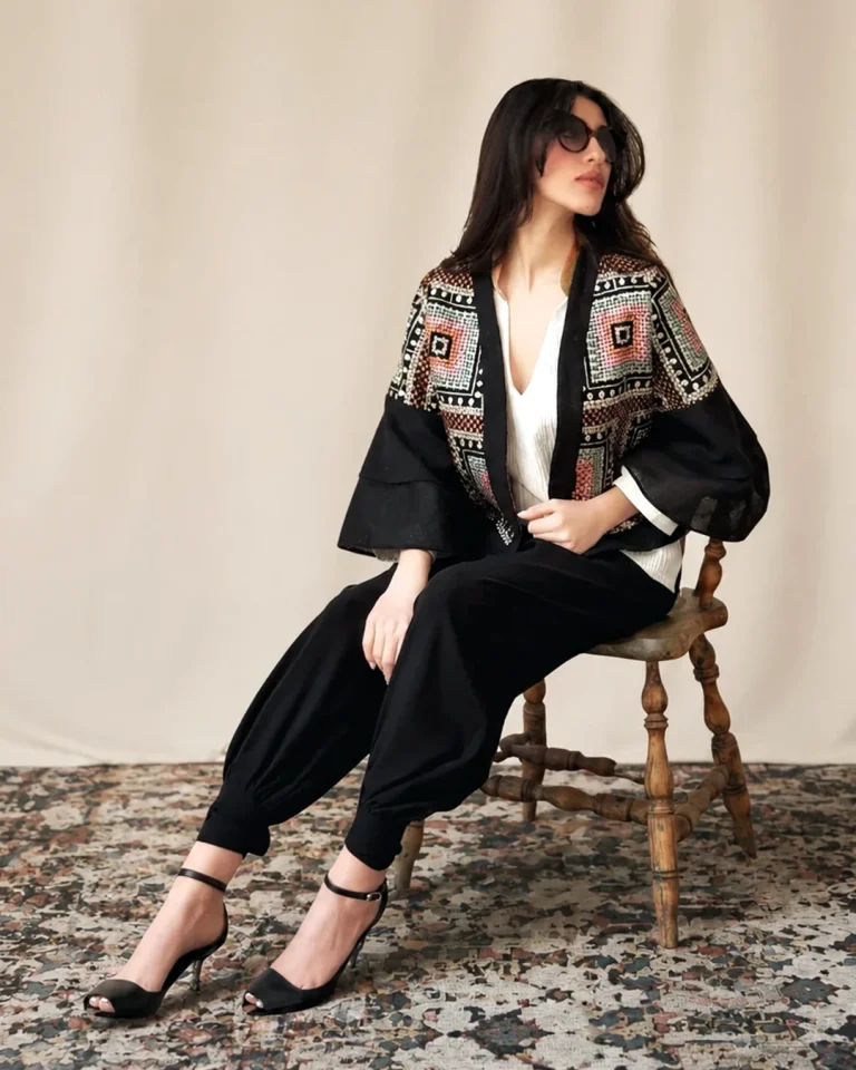 Seated full-body view of the Kajideh Jacket paired with Lenga crepe trousers, showing voluminous sleeves and gathered hems