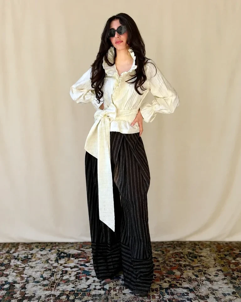 Full-length view of the Queen taffeta blouse and trousers with a light belted top and dark relaxed striped trousers