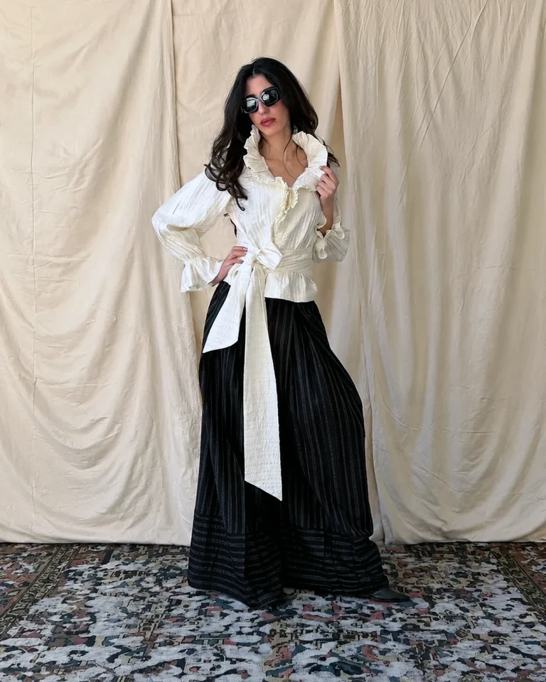 Full-length view of Look 10 featuring a light blouse with a standing ruffled collar, long sash belt, and wide striped trousers