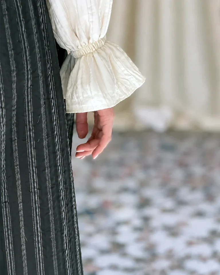 Close-up view of the Queen taffeta trousers with dark vertical stripes and a light gathered blouse cuff
