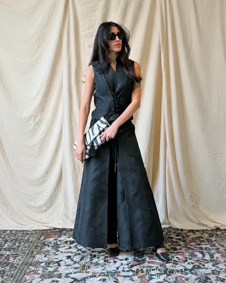 Full-length view of Look 11 Sika; a black taffeta vest and culottes set styled with a clutch and heels.