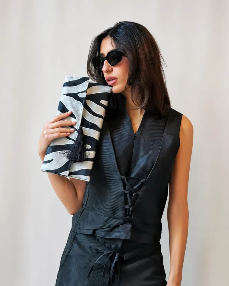 Close-up of the black Sika vest with lace-up detailing and a black-and-white clutch from the Cusp collection.