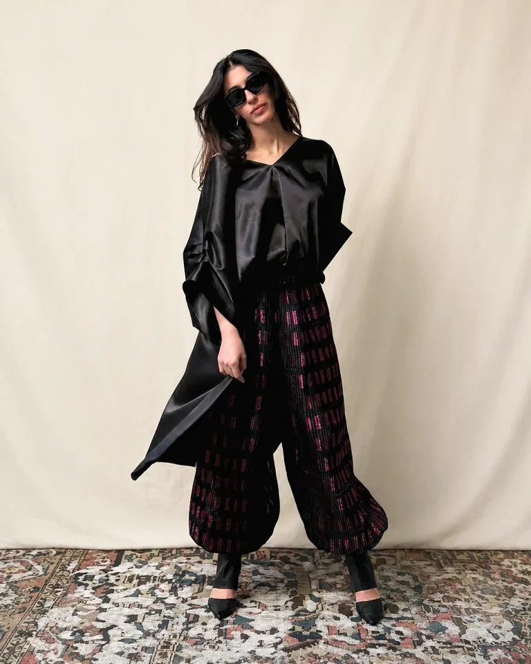 Full-length view of the Roham look with a black silk blouse and voluminous pleated organza trousers with a deep magenta sheen