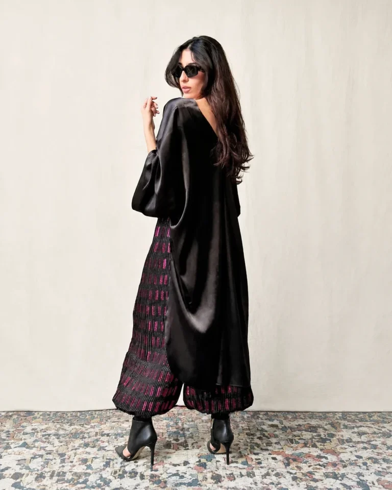Back view of the Roham look with a long black silk blouse and pleated organza trousers featuring vertical texture and wide volume