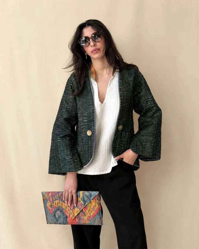Full-length view of the reversible Saro Jacket in dark handwoven textile with artisanal engraved buttons, styled with a white blouse, dark trousers, and a patterned clutch