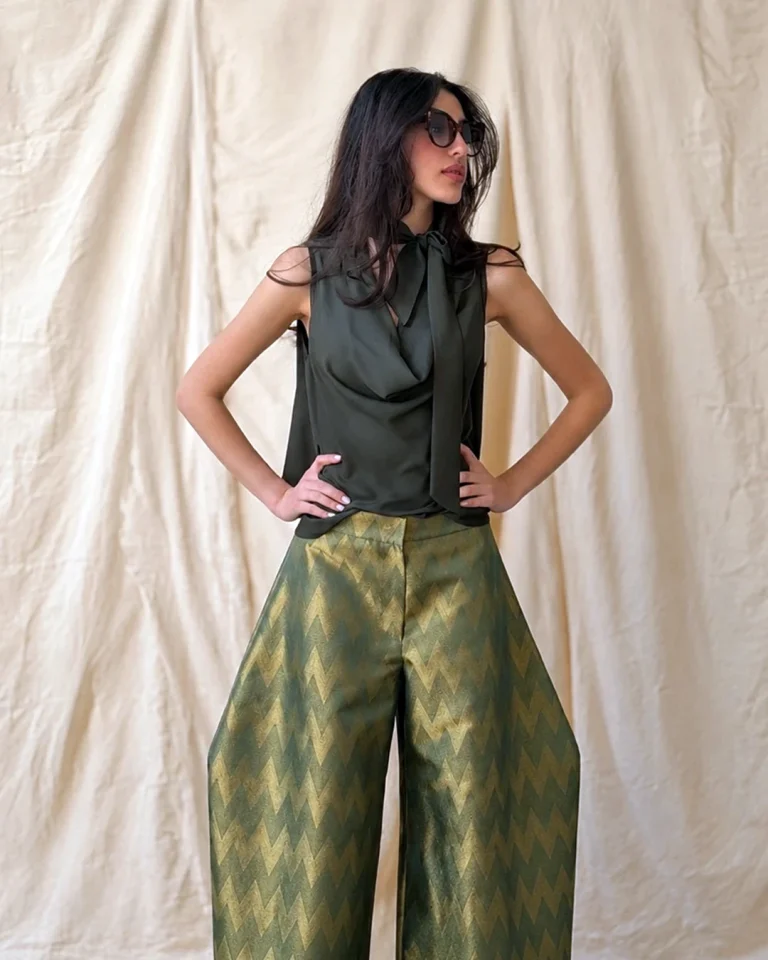 Close-up of Look 18 from the Cusp collection, featuring the dark green Zarrin blouse with a tie-neck detail and green-gold patterned trousers