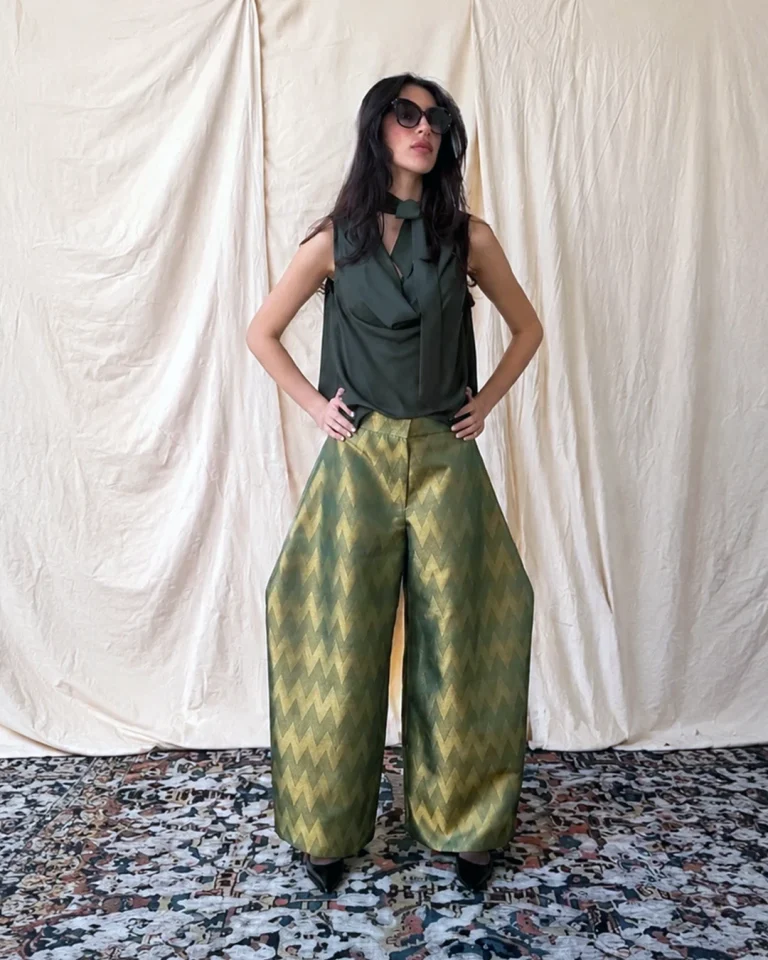 Full-length view of the Zarrin blouse and trousers from the Cusp collection, with a dark green blouse and wide glossy trousers with a gold geometric pattern