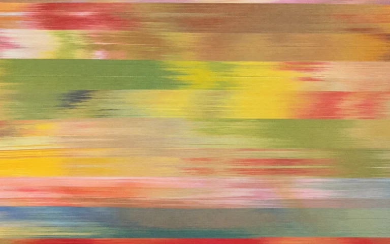 Close-up of hand-woven Persian Ikat silk fabric, known as Daraayi from Yazd, showing colorful horizontal bands in muted tones of yellow, olive green, pink, beige, and blue with characteristically soft, blurred edges created through the traditional resist-dyeing technique.