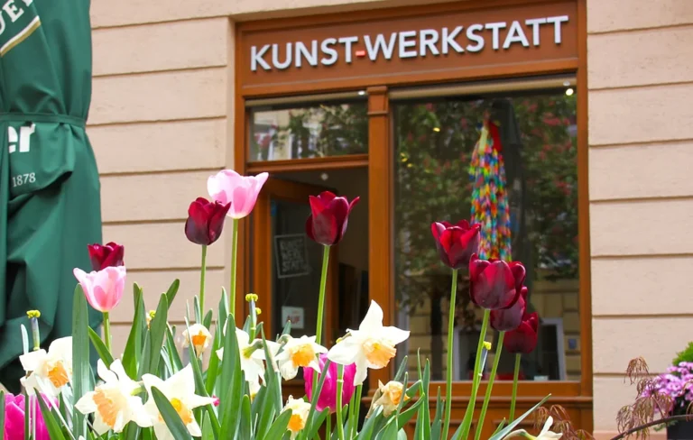Entrance to Kunst-Werkstatt in Munich, with flowers in the foreground and the gallery sign above the door.
